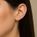 Close-up of an ear wearing a gold hoop earring with a neutral background