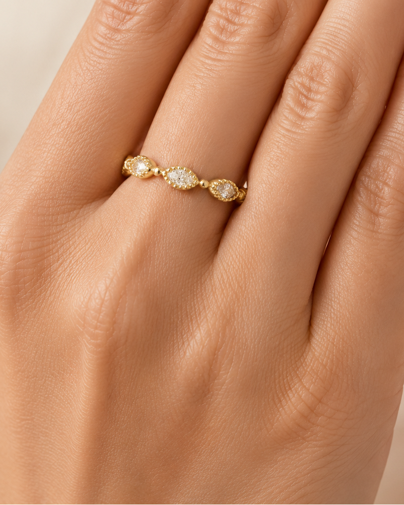 Gold ring with small stones on a hand against a beige background