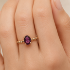 Gold ring with a purple gemstone on a hand against a neutral background