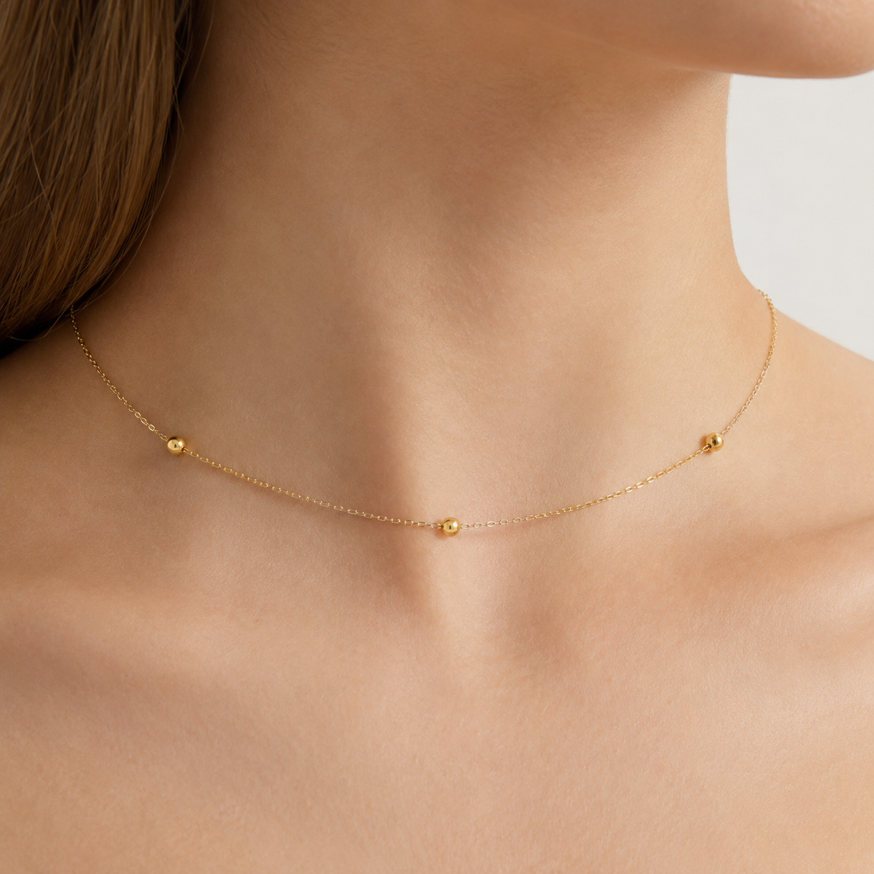 Gold necklace on a person's neck with a plain background