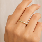 Gold ring with small diamonds on a hand against a neutral background