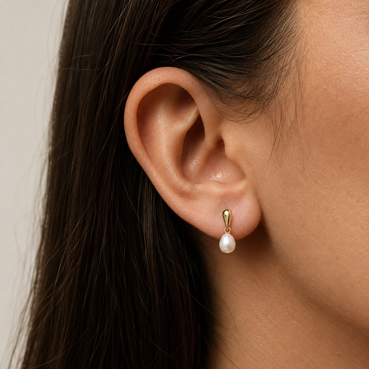 Close-up of an ear wearing a pearl earring with a neutral background