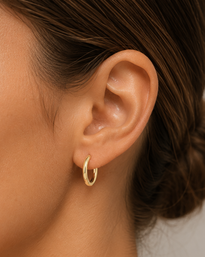 Close-up of a person wearing a gold hoop earring with a neutral background