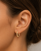 Close-up of a person wearing a gold hoop earring with a neutral background