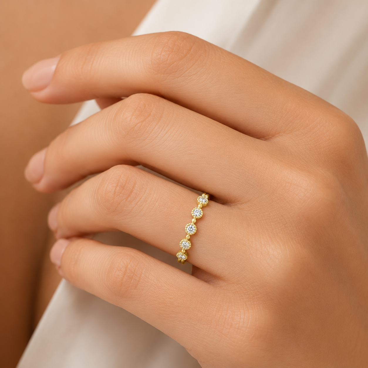 Gold ring with diamonds on a hand against a neutral background