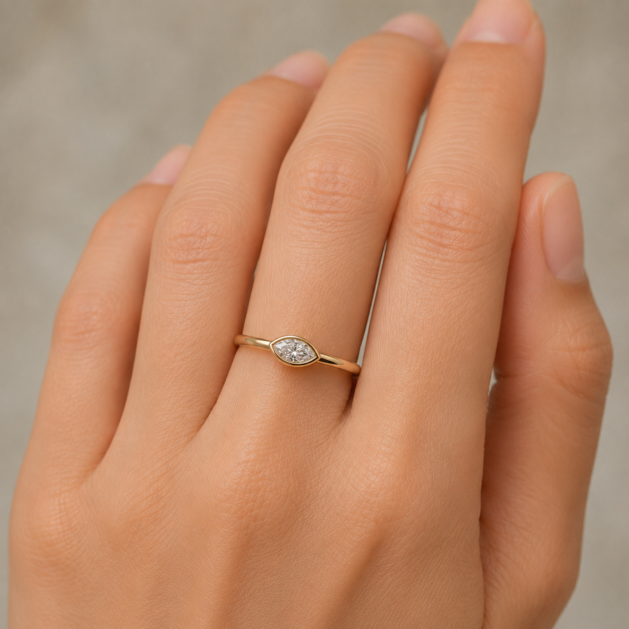 Gold ring with a diamond on a person's finger against a neutral background