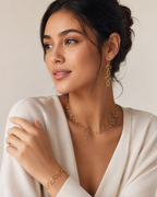 Woman wearing gold jewelry including earrings and a necklace, with a plain background