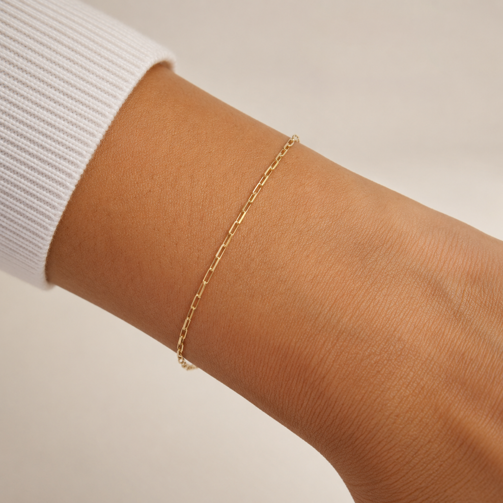 Gold chain bracelet on a wrist with a neutral background