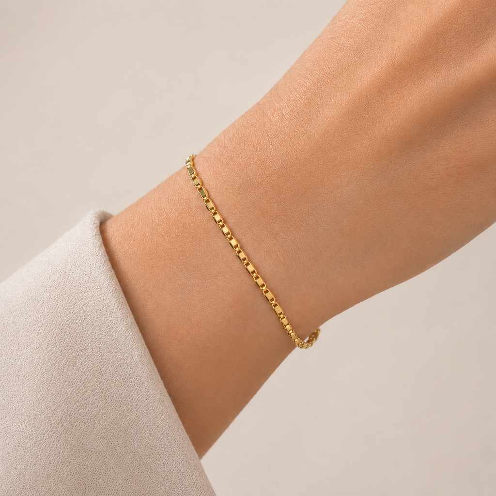Gold bracelet on a person's wrist against a neutral background