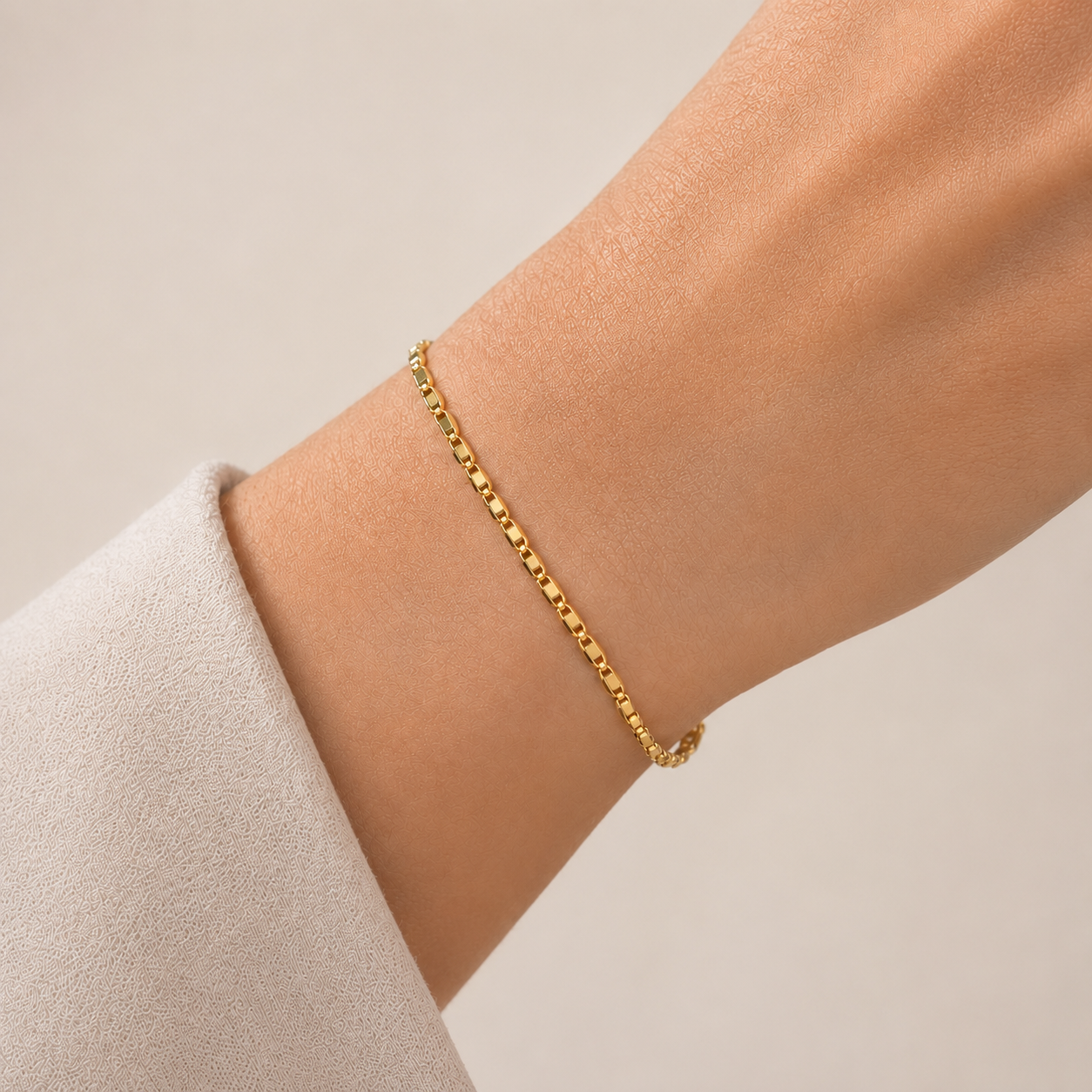 Gold bracelet on a person's wrist against a neutral background