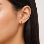 Close-up of an ear wearing a gold earring with red stones on a neutral background