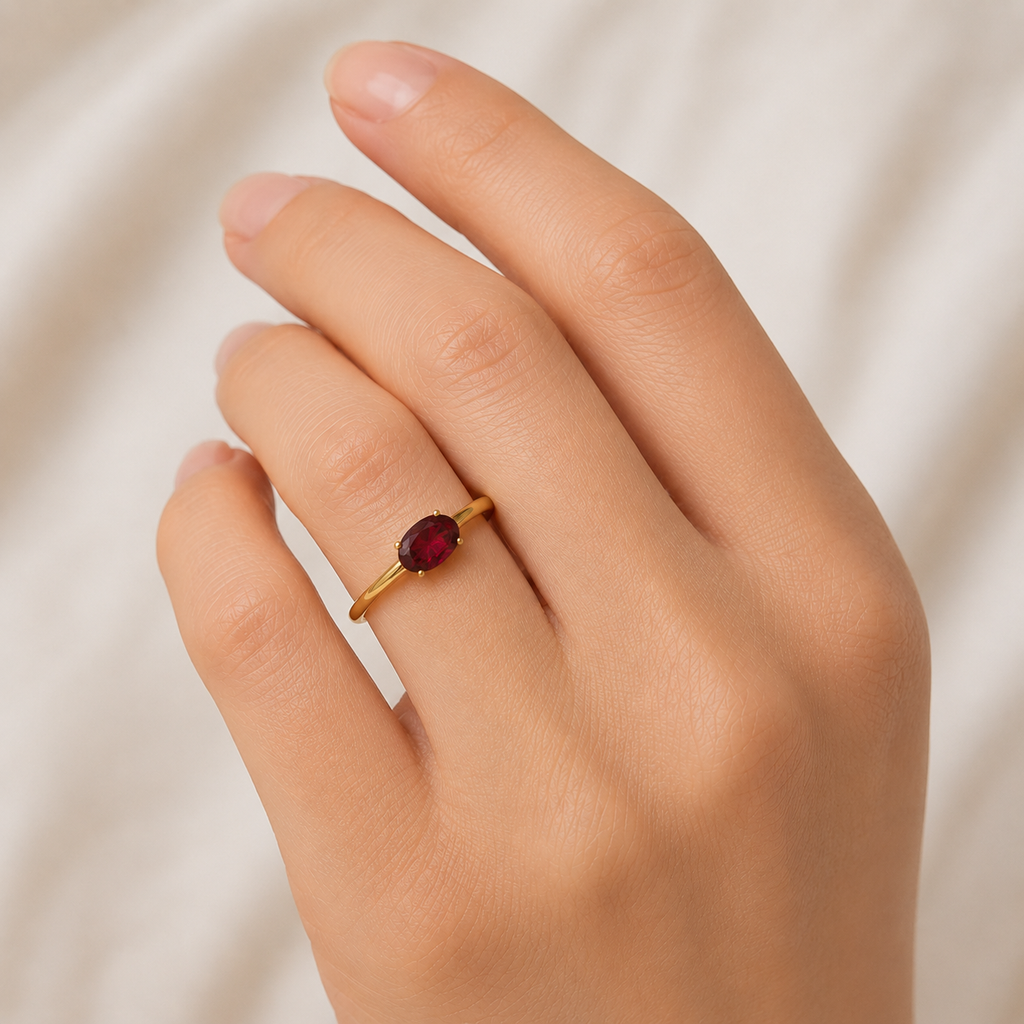 Gold ring with a red gemstone on a hand against a neutral background