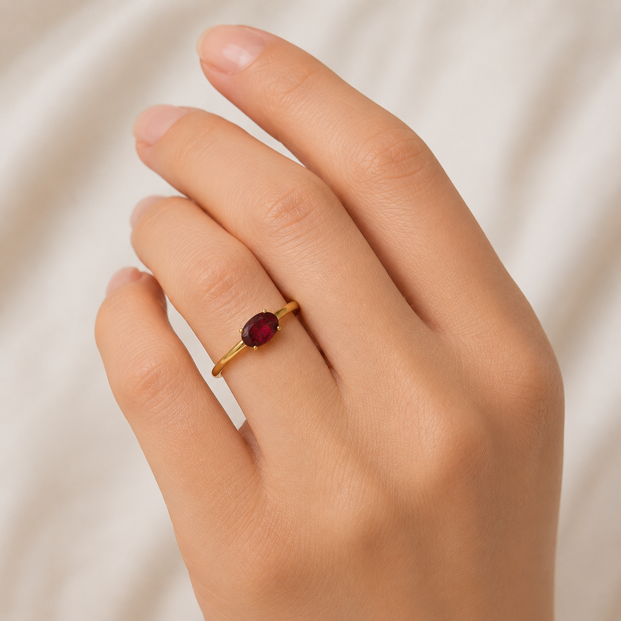 Gold ring with a red gemstone on a hand against a neutral background