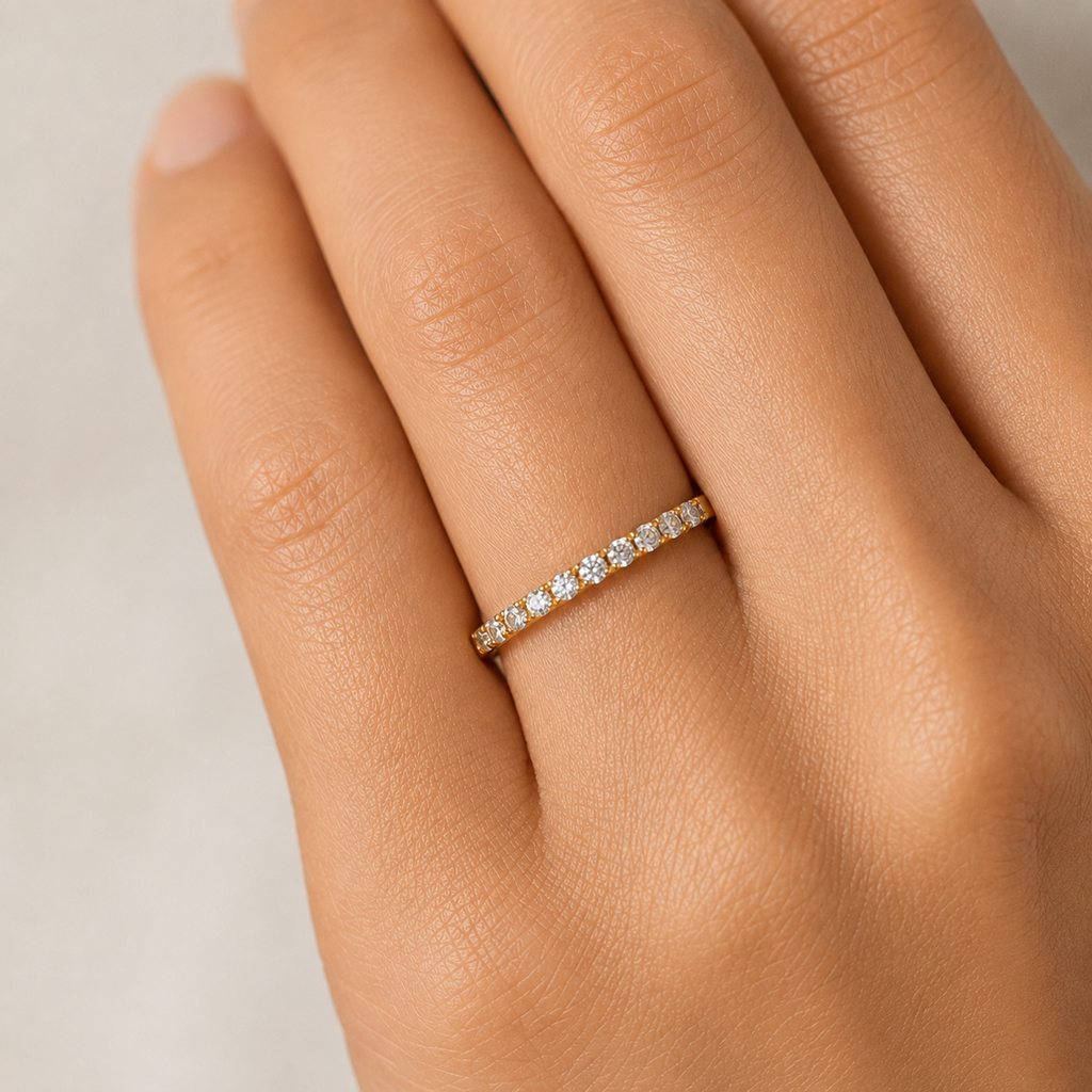 gold ring with small diamonds on a hand against a neutral background