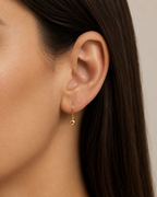 Close-up of an ear wearing a gold earring with dark hair and neutral background